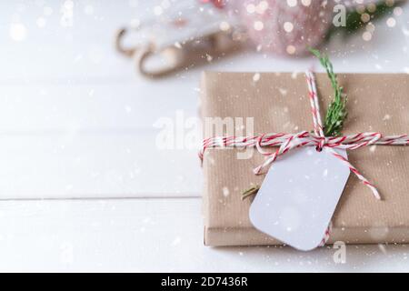 Christmas eco gift with empty tag. Glowing snow bokeh, coniferous branch. Winter holidays mock up on white background. Zero waste, plastic free Stock Photo