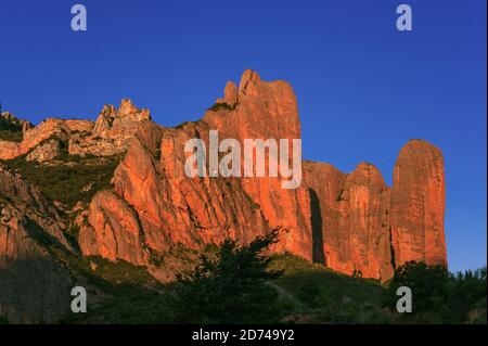 The majestic Mallos de Riglos, a spectacular natural gateway to the Pyrenees, glow bright orange-red in evening sunlight in Huesca Province, Aragon, Spain.  Los Mallos (The Mallets) formed at least 20 million years ago, when material washed down from Pyrenean slopes compacted with limestone to form conglomerate rock.  The distinctive ‘mallets’, sculpted by erosion, are a physical border between the Pyrenean foothills and the Ebro Basin, rising to around 300 m (980 ft).  In the 11th century, the Mallos area was briefly an independent kingdom after Pedro, King of Aragon, gave it as a dowry. Stock Photo