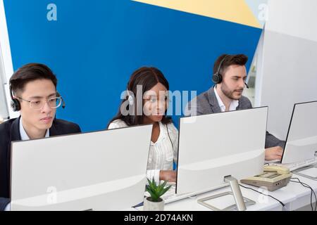 Focused call center operators with headsets working in front of computer monitors at open space office Stock Photo