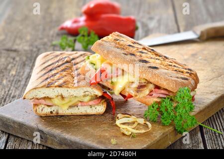 Grilled Italian ciabatta bread with ham, cheese and vegetables served on a wooden cutting board Stock Photo