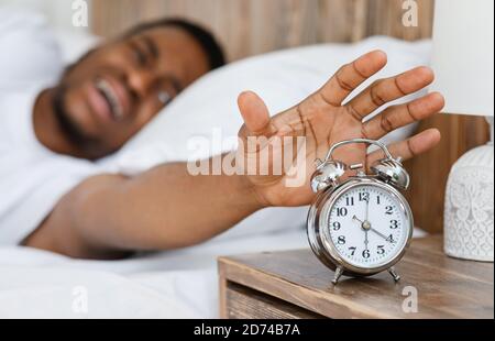 African Guy Turning Off Alarm Clock Waking Up At Home Stock Photo