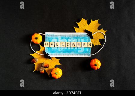 Halloween pumpkins, protective medical mask and yellow maple leaves on a black background, bats made of black paper. The inscription HALLOWEEN The Stock Photo