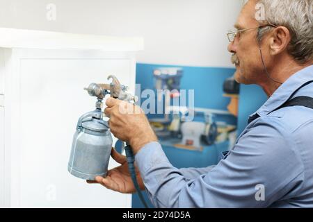 A pensioner with gray hair and glasses paints metal products. Additional earnings for an elderly person Stock Photo