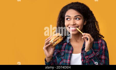 Funny African American Lady Eating Burger And French Fries Stock Photo