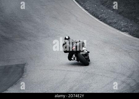 man riding motorcycle in asphalt road. Motorcyclist at black sport motorcycle. View from back. Stock Photo