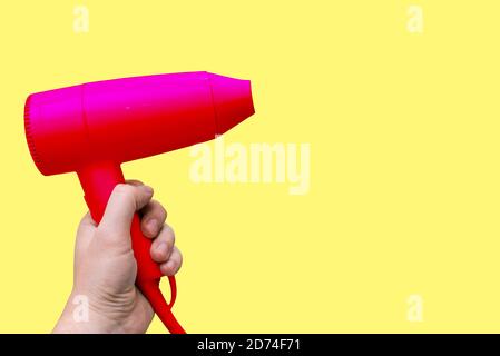 Red electric hair dryer in the hands of a man, isolated on a yellow background with a copy of the space. Modern device for drying, styling and cutting Stock Photo
