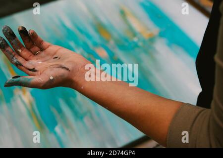 Woman artist's hand covered in paint, abstract art in background. Horizontal composition, full frame, focus on foreground. Stock Photo