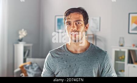 Sweating Muscular Athletic Fit Man in Grey Outfit is Posing After a Workout at Home in His Spacious and Sunny Living Room with Minimalistic Interior. Stock Photo