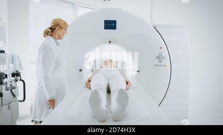 In Medical Laboratory Female Radiologist Controls MRI or CT Scan with Female Patient Undergoing Procedure. High-Tech Modern Medical Equipment.  Stock Photo