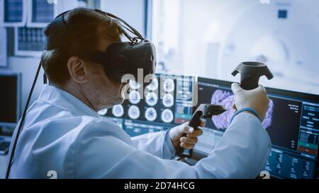 Futuristic Concept: In Medical Laboratory Surgeon Wearing Virtual Reality Headset Uses Controllers to Remotely Operate Patient with Medical Robot Stock Photo