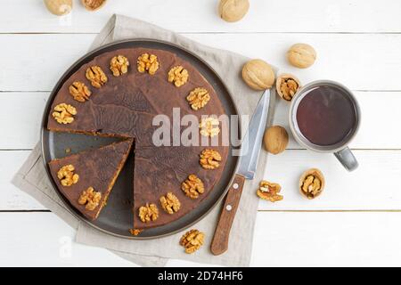 Homemade Walnut Cake with Chocolate Icing and mug of hot tea on white wooden table. Top view. Stock Photo