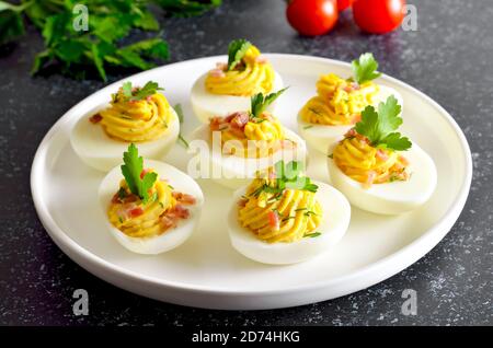 Deviled stuffed eggs with egg yolk, bacon, mustard and parsley on dark stone background, close up view Stock Photo