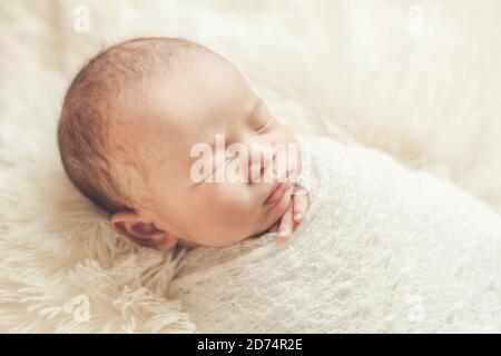 Adorable newborn baby sleeping in cozy room. Cute happy infant baby portrait with sleepy face in bed. Soft focus at the baby eyes. Newborn nursery Stock Photo