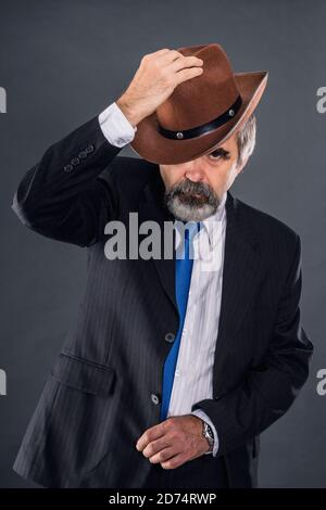 Elderly expressive dandy man in a suit with a tie aggressively steps and takes off his hat Stock Photo