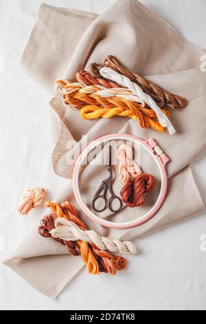 Set for embroidery. Linen fabric, patterns for embroidery, hoop, thread of yellow and brown colors and needles. Copy space, top view Stock Photo