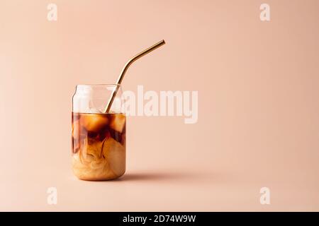 Glass of iced coffee in tall glass with golden straw with cream on pastel background for your design. Food concept in vintage style. Copy space. Closeup. Stock Photo