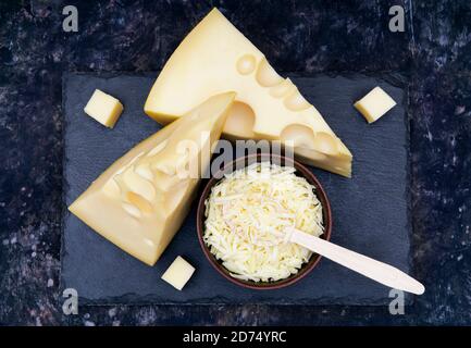 Two cheese wedges and a bowl of grated cheese on a black stone board Stock Photo