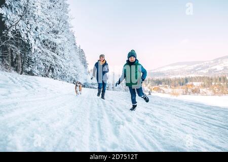 Mother and son having a fun during dog walk. They running with their beagle dog in snowy forest. Mother and son relatives and femily values concept im Stock Photo