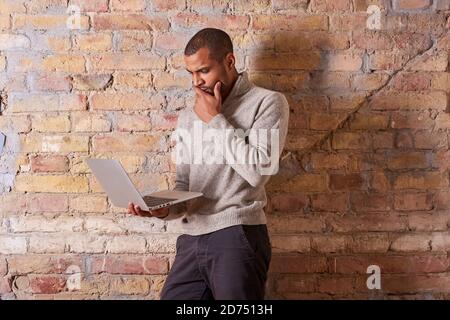 A serious handsome young man using a laptop in a sweater. Stock Photo