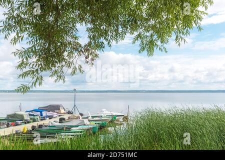 Long pier with moored boats on river with reeds on bank Stock Photo
