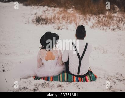 groom and bride sitting on a Mexican national veil on a snowy hill Stock Photo