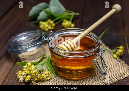 Jar with linden honey with stick for honey and fresh linden flowers on a wooden table. Stock Photo