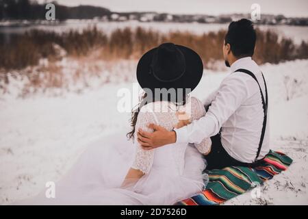 groom and bride sitting on a Mexican national veil on a snowy hill Stock Photo
