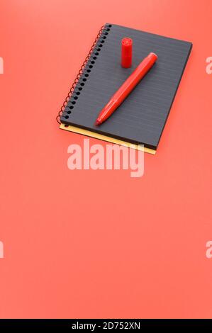 Vertical shot of a black notebook and a red marker on a red surface Stock Photo