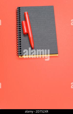 Vertical shot of a black notebook and a red marker on a red surface Stock Photo