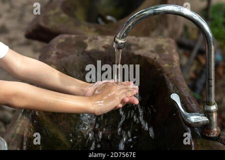 Hygiene concept cleaning hand and washing hands in the public park. A boy washes his hands with soap in the wooden basin. Stock Photo