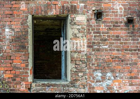 Destroyed window opening on a red brick wall in an old abandoned house. Stock Photo