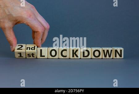 Symbol for a second lockdown. Hand turns cubes and changes the expression '1st lockdown' to '2nd lockdown'. Beautiful grey background. Medical and cov Stock Photo