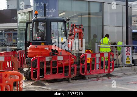 ground worker or builders working on a pavement next to a digger surrounded by barriers Stock Photo