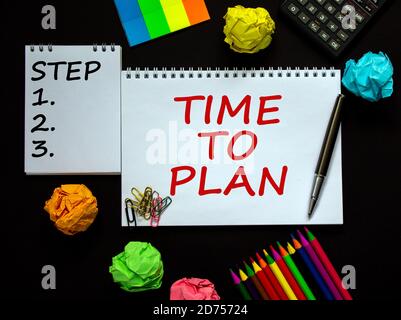 White notes with inscription 'time to plan' and 'step 1, 2, 3' on beautiful black table, colored paper, colored pencils, paper clips, pen and calculat Stock Photo
