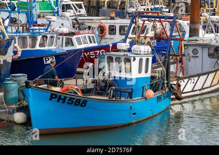 Two fishermen talking on a fishing trawler that is docked on a quayside Stock Photo