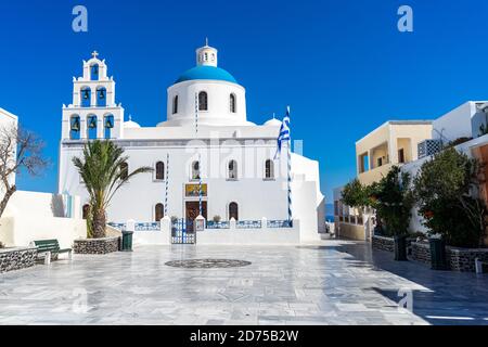 Orthodox church in Oia, Santorini, Greece on a summer day with greek flag. beautiful clear blue sky. Stock Photo