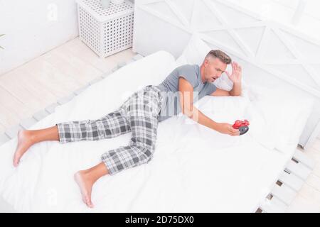 time is gone. stressful man wake up turn off the alarm clock. Time to wakeup. Tired unhappy man in bed. man suffering from headache. terrible loud noise. insomnia and sleep disorder. daily routine. Stock Photo