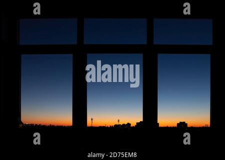 Through triple window POV with scenic city downtown cityscape black building silhouettes against fiery orange to blue dramatic sunset or sunrise on Stock Photo