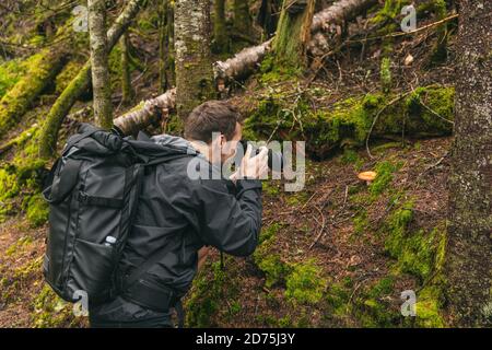 Nature still photography photographer man with professional slr camera taking picture of wild mushroom in forest during trail hike Stock Photo