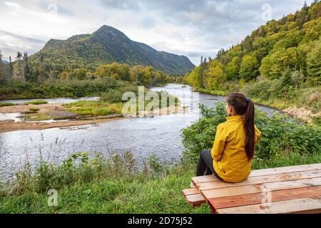 Camping nature woman sitting at picnic table enjoying view of wilderness river in Quebec and autumn foliage forest, Canada travel. Parc de la Jacques Stock Photo