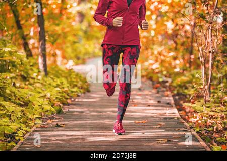 Run path woman running in forest park nature outdoors fitness workout on boardwalk in autumn fall foliage wearing red activewear outfit clothing. Girl Stock Photo