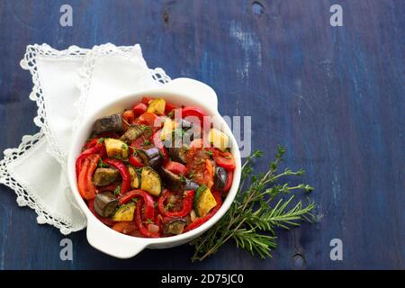 Ratatouille, a traditional French dish of fresh vegetables in a white ceramic bowl on a dark blue background Stock Photo