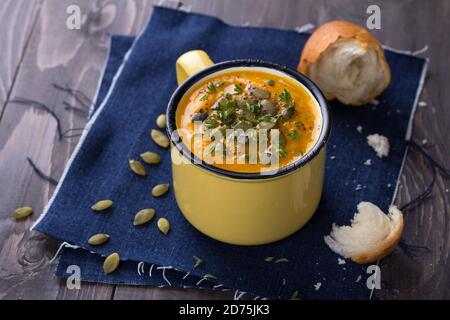 Pumpkin soup with pumpkin seeds and thyme in the cup on a wooden surface Stock Photo