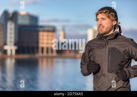 Winter running athlete man jogging outdoor in city outside wearing cold weather accessories - hat ,gloves , windproof sport jacket. Active healthy Stock Photo