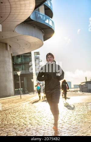 Winter running man wearing cold weather activewear outerwear clothes training outside. Male athlete city urban jogging outside on Europe street Stock Photo