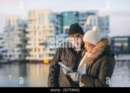Phone couple using mobile on winter city walk walking outside on street looking up directions on online app. Happy Asian woman and Caucasian man Stock Photo