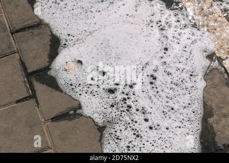 Foam streams on the asphalt from car wash, wet concrete texture. Backdrop background. Intricate natural patterns of foam and soap bubbles. Black tarma Stock Photo