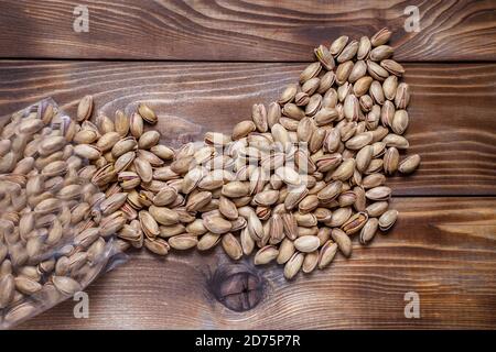 Plastic bag with pistachios on a wooden background. Nuts are scattered on the surface. Flat layout Stock Photo