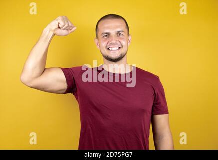 Russian man wearing basic red t-shirt over yellow insolated background showing arms muscles smiling proud Stock Photo