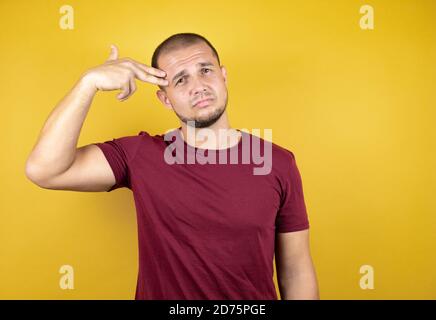 Russian man wearing basic red t-shirt over yellow insolated background Shooting and killing oneself pointing hand and fingers to head like gun, suicid Stock Photo